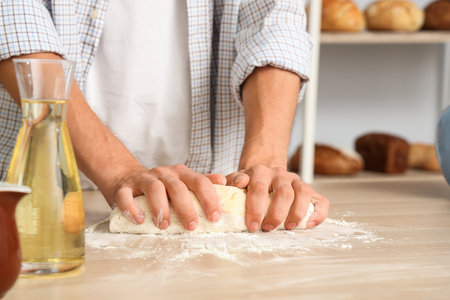 Young man preparing dough for fresh buns at table in kitchen, closeupの写真素材