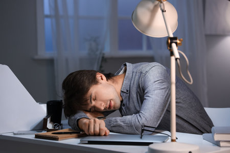 Sleeping young businessman working in office at nightの写真素材