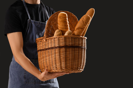 Handsome young man with basket full of fresh baguettes on black backgroundの写真素材