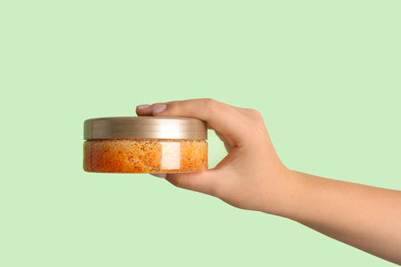 Female hand with jar of natural body scrub on color background, closeupの写真素材