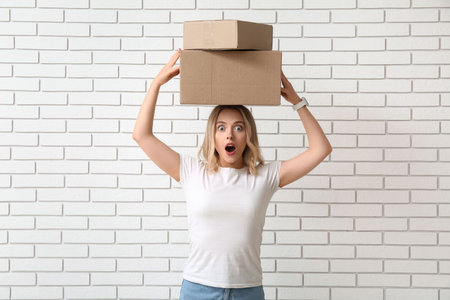 Emotional young woman with cardboard boxes on white brick background