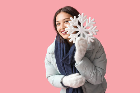 Beautiful young Asian woman in warm scarf and gloves with snowflake on pink backgroundの写真素材