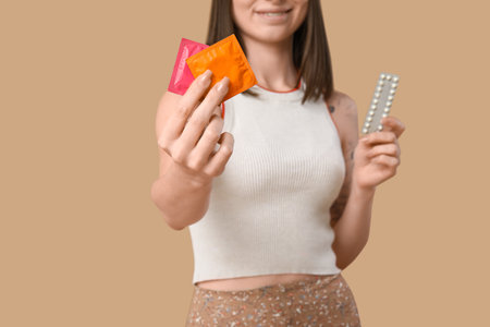 Beautiful young woman with contraceptive pills and condoms on brown background. AID awareness conceptの写真素材