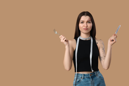 Beautiful young sporty woman with measuring tape and cutlery on brown background. Weight loss...