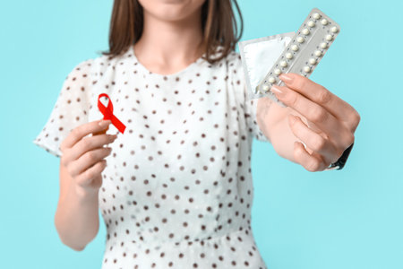 Beautiful young woman with contraceptive pills, red ribbon and condom on blue background. AID awareness conceptの写真素材