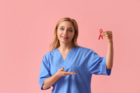 Mature female doctor with red ribbon on pink background. World AIDS Day conceptの写真素材