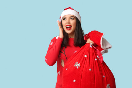 Pretty young woman with bag of Christmas gifts on blue backgroundの写真素材