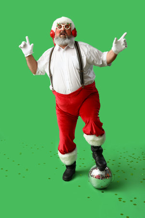 Funny Santa Claus in headphones with disco ball listening to music and dancing on green backgroundの写真素材