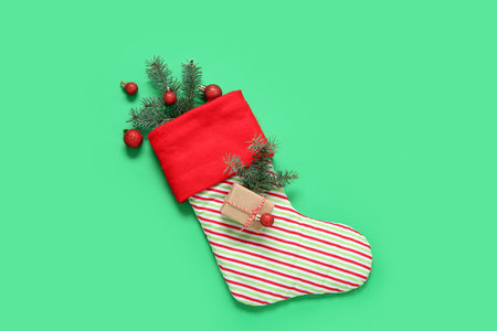 Christmas sock with fir branches, balls and gift box on green backgroundの写真素材