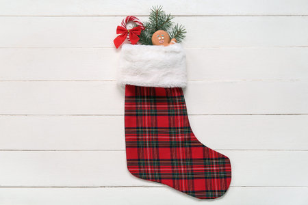 Christmas sock with fir branch, gingerbread and candy cane on white wooden background