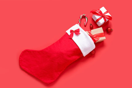 Christmas sock with balls, gift boxes and candy cane on red background