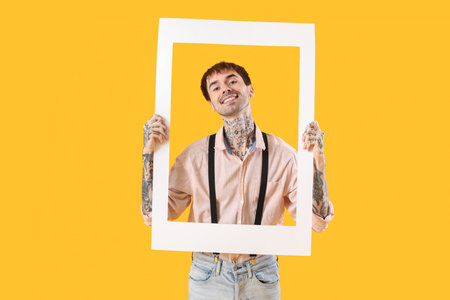 Happy young man holding white photo frame on yellow backgroundの写真素材