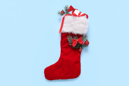 Christmas sock with fir branches, balls and gift box on blue background