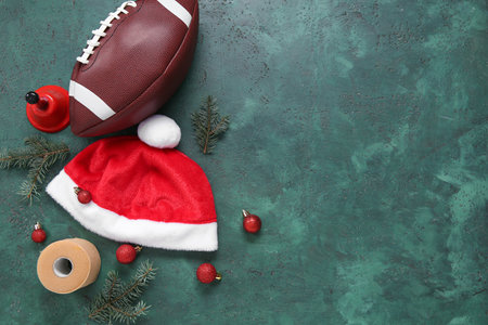 Rugby ball with Santa hat, fir branches and Christmas bell on green backgroundの写真素材