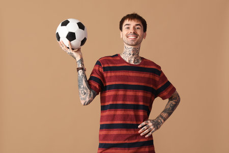 Happy young man with soccer ball on brown background
