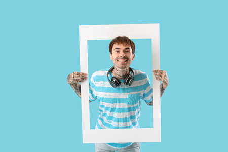 Happy young man holding white photo frame on blue backgroundの写真素材