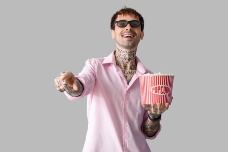Happy young man with popcorn watching movie on gray backgroundの写真素材