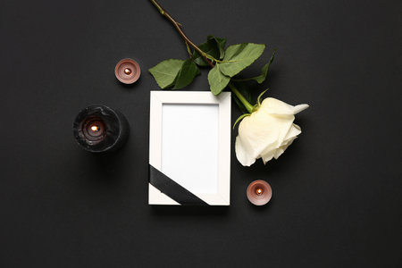Beautiful white rose, candles and photo frame on black backgroundの写真素材