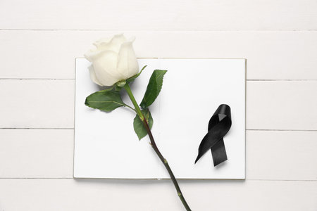 Rose with black ribbon and blank open notebook on white wooden backgroundの写真素材