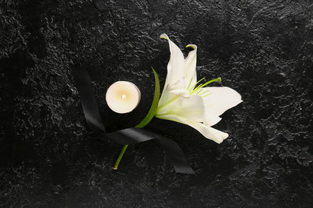 Beautiful lily with burning candle and ribbon on black grunge backgroundの写真素材
