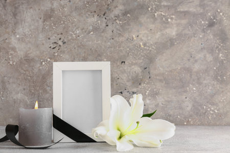 Photo frame with white lily, black ribbon and burning candle on gray grunge backgroundの写真素材