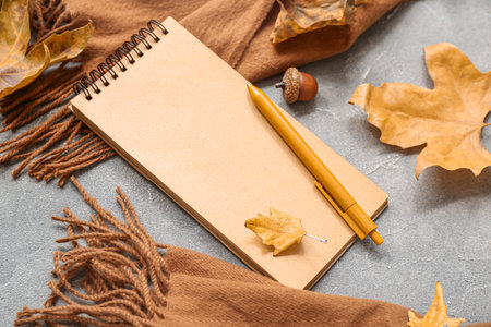 Notebook with pen, warm plaid and autumn leaves on gray grunge background