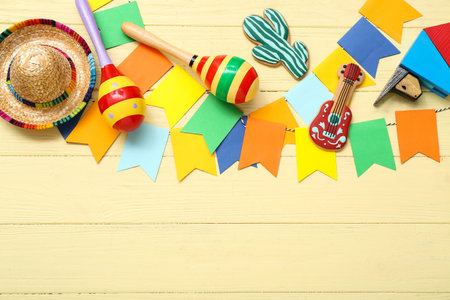 Maracas, garland and sombrero on yellow wooden background. Mexico's Independence Day celebration