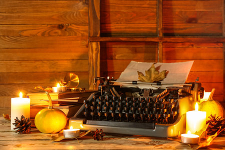 Vintage typewriter, burning candles, pumpkins, pine cones, books and autumn leaves on wooden backgroundの写真素材