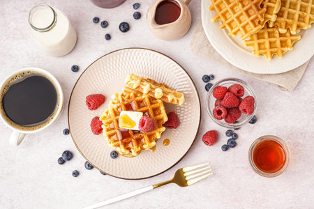Tasty waffles with berries, maple syrup, milk and cup of coffee on white backgroundの写真素材