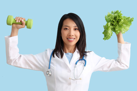 Female Asian nutritionist with lettuce and dumbbell on blue backgroundの写真素材