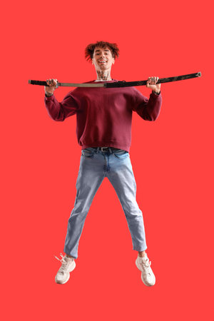 Tattooed young man with sword jumping on red backgroundの写真素材