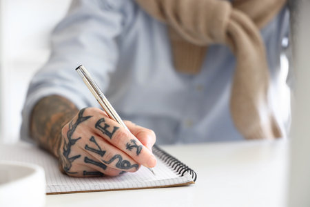 Handsome young tattooed businessman writing in notebook at office