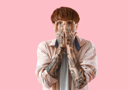 Afraid young tattooed man on pink backgroundの写真素材