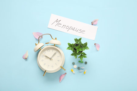 Word MENOPAUSE with alarm clock, pills and petals on blue backgroundの写真素材