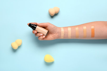 Female hand with bottle of makeup foundation, sponges and samples on blue backgroundの写真素材