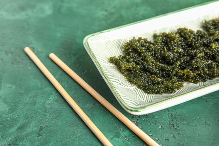 Plate with healthy seaweed and chopsticks on green background, closeup