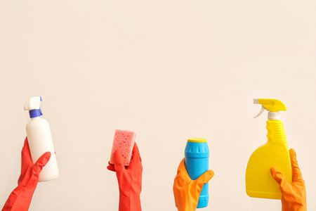 Female hands in rubber gloves holding cleaning supplies on beige backgroundの写真素材