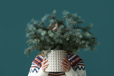 Woman holding vase with beautiful fir tree branches on green backgroundの写真素材