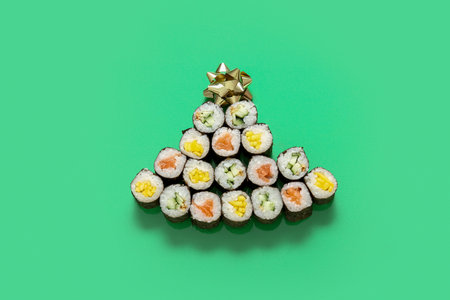 Christmas tree made of tasty sushi rolls on green background