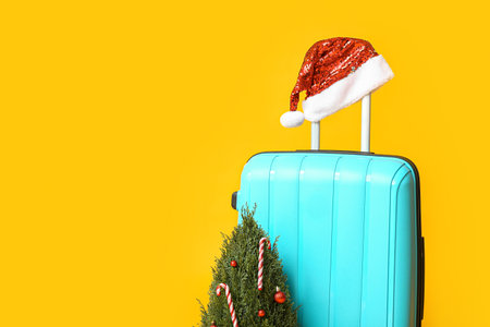 Suitcase with Santa hat and Christmas tree on yellow backgroundの写真素材