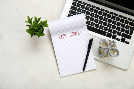 Notebook with text 2024 GOALS, laptop and houseplant on white grunge background
