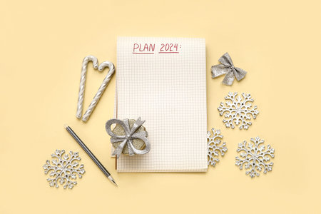 Notebook with text PLAN 2024, pen and Christmas decorations on light yellow background