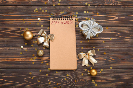 Notebook with text 2024 GOALS, golden Christmas decorations and confetti on wooden background