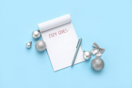Notebook with text 2024 GOALS, pen and silver Christmas balls on blue backgroundの写真素材