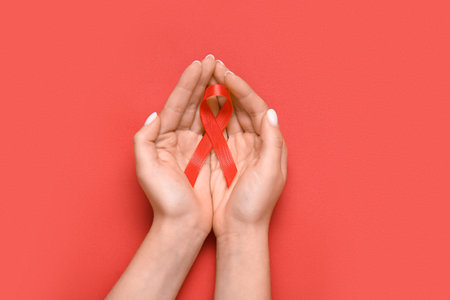 Female hands with red ribbon on color background. AIDS Day concept