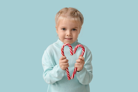 Cute little girl with Christmas candy canes on blue background