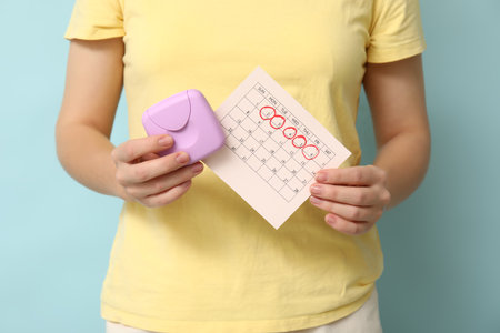 Young woman with tampon box and calendar on blue background, closeupの写真素材