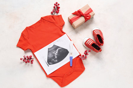 Composition with baby clothes, sonogram image, Christmas gift and decorations on light backgroundの写真素材