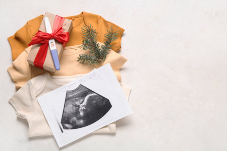 Composition with baby clothes, sonogram image, pregnancy test and Christmas gift on light backgroundの写真素材