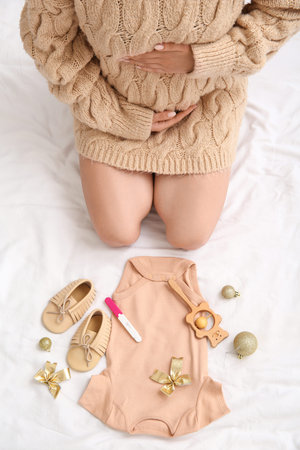 Pregnant woman with baby accessories, test and Christmas decorations on bed